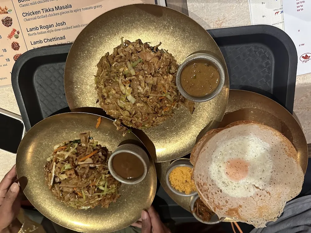 Two plates of kottu and an egg hopper set on a tray