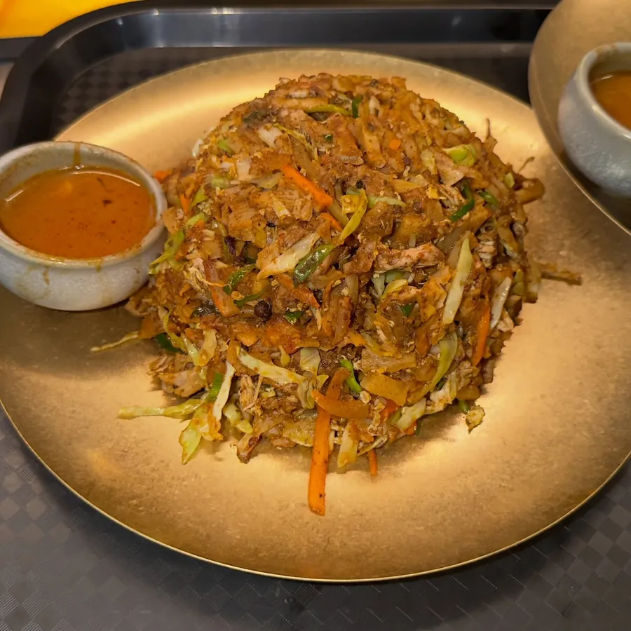 Chicken kottu roti on a brass plate with curry gravy